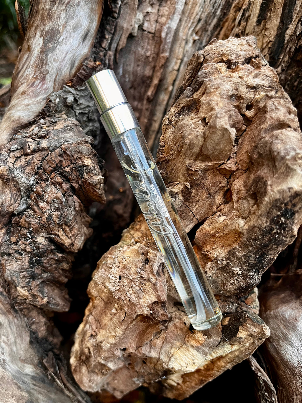 Clear glass perfume vial with silver cap on a textured wooden surface