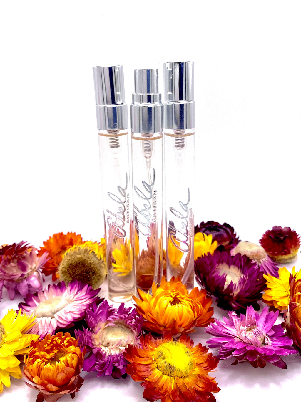 Three  perfume bottles with silver caps surrounded by colorful flowers on a white background